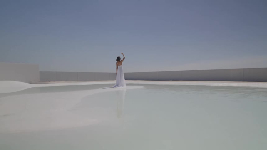 Woman in long white dress is standing in the center of a flat white landscape of a lake
