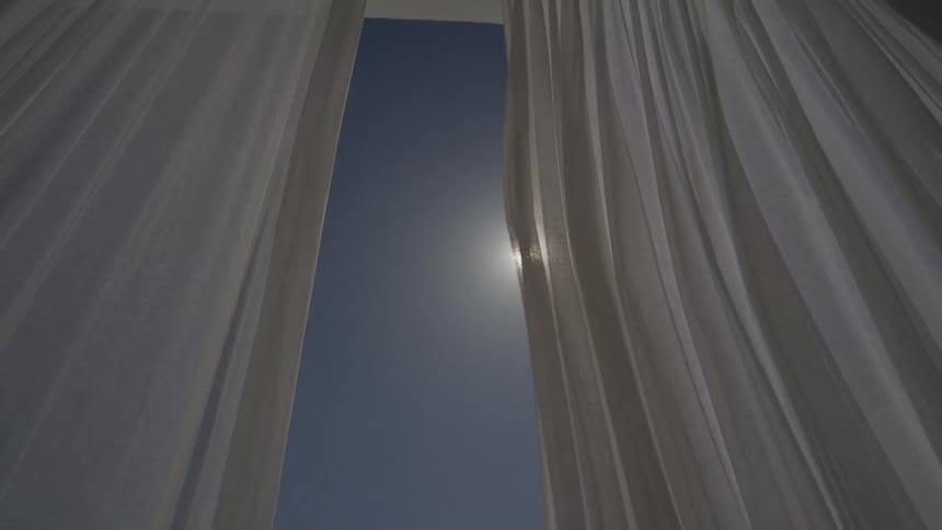 A curtain on a window overlooking the blue sky and the sun shining brightly