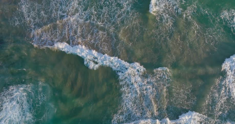 Aerial view of the foamy waters of the ocean reaching the sand of the beach
