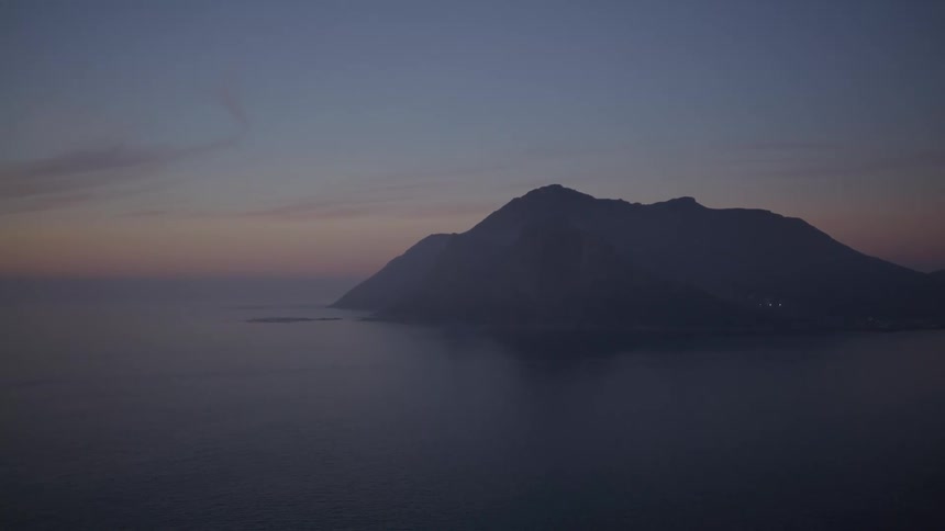 A large mountain of a crust with a calm sea in a dusk