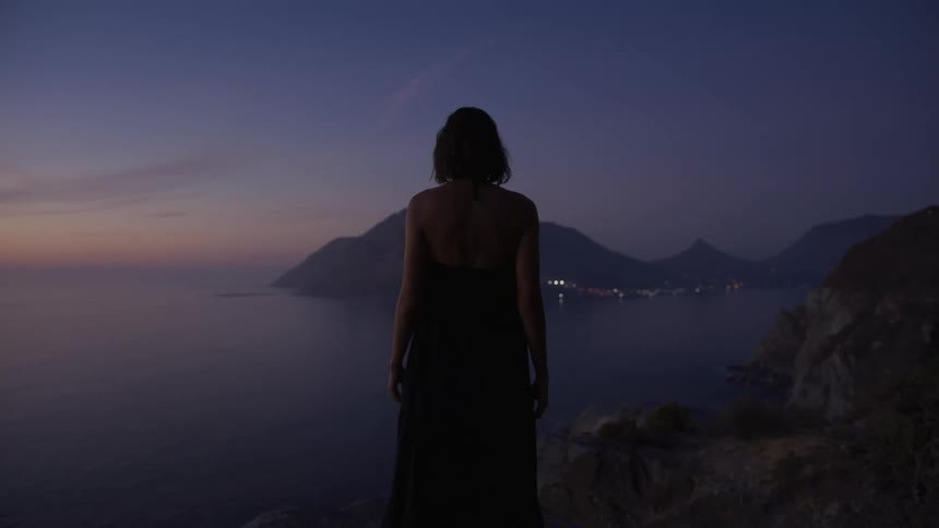 Woman in a dress walking on a rock by the sea on a morning sky with red and purple tones
