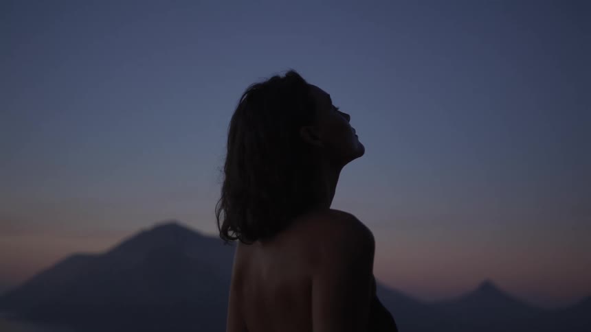 Woman looking up with the silhouette of mountains on the horizon on a morning with a purple sky