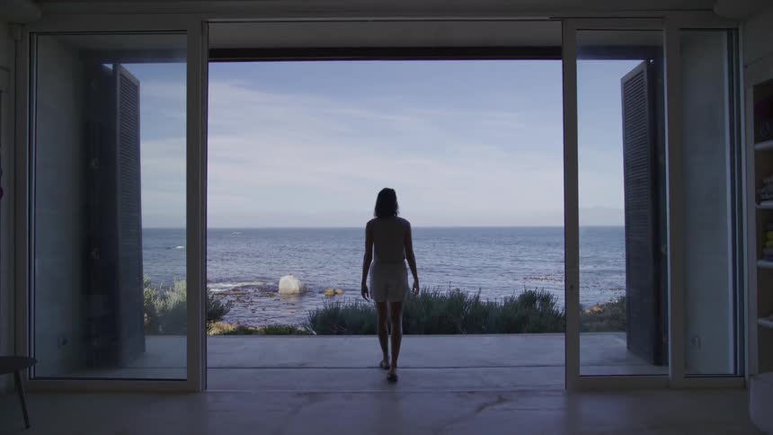 Back view of a woman walking towards a glass door with a view of the sea