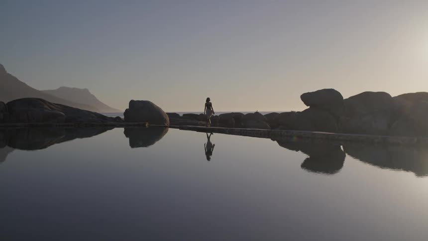 Woman walking along the edge of a lake and rocks in a natural environment at dawn