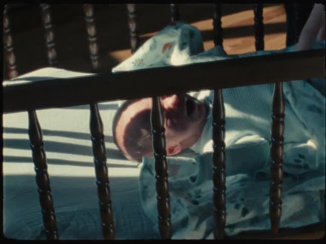 Newborn baby crying in the crib and a pair of hands pulling the blanket off