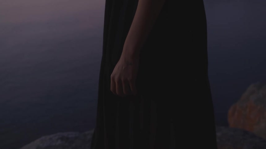 Woman wearing a long dress standing on a rocky cliff by the sea