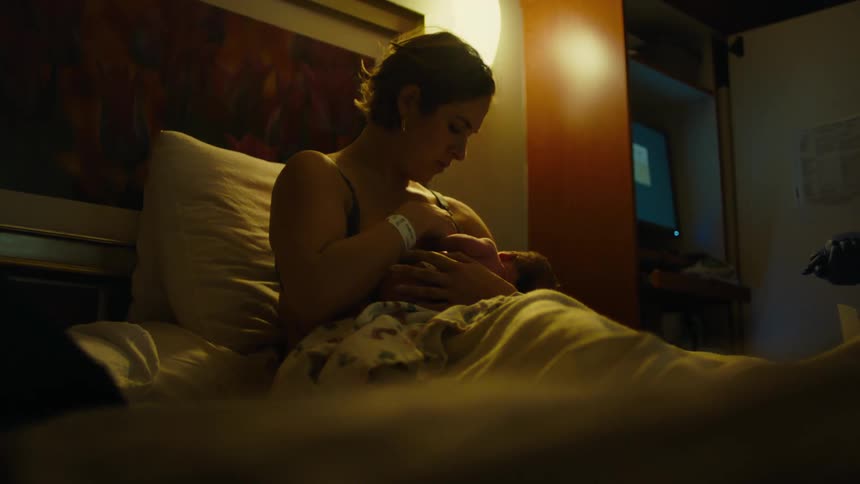 Mother sitting on a bed breastfeeding her newborn baby