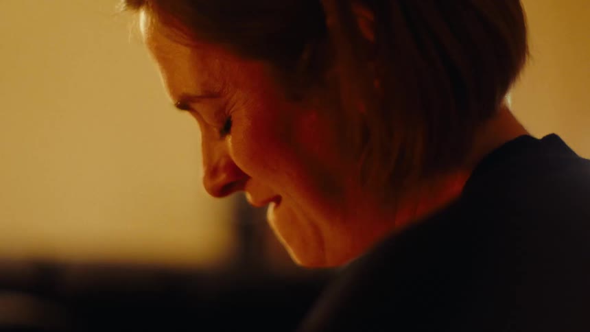 The face of a woman who is biting her lower lip and there is a strong orange light in the room