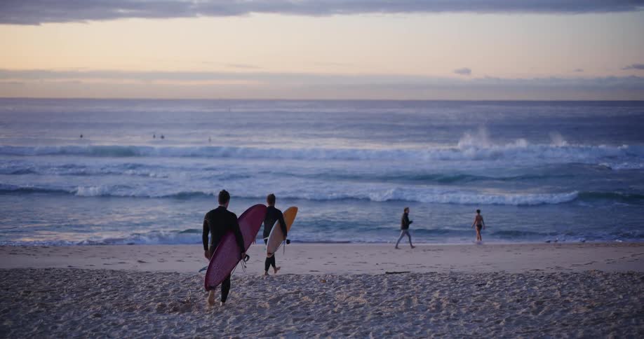 Surfers with their surfboards walking on the sand towards the sea at the beach