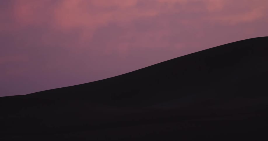 Silhouette of a desert dune against a sky in shades of red and purple