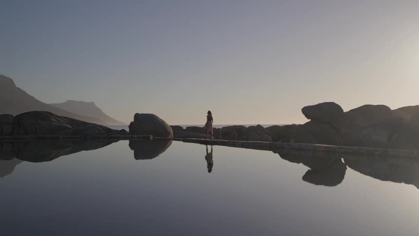 A person walking beside a lake and his image is reflected in the surface of the water of a still lake