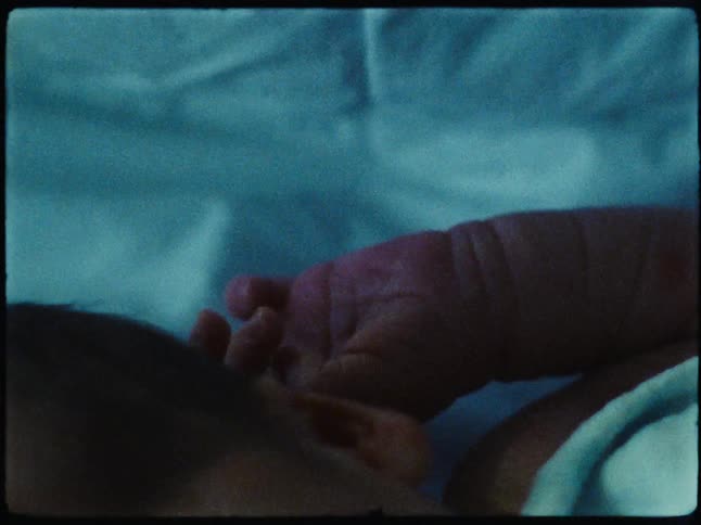 Sleeping baby covered by a baby blanket moves a hand