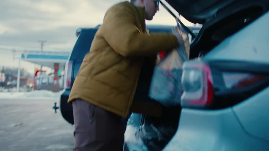 A man loading groceries on the trunk of a car at evening