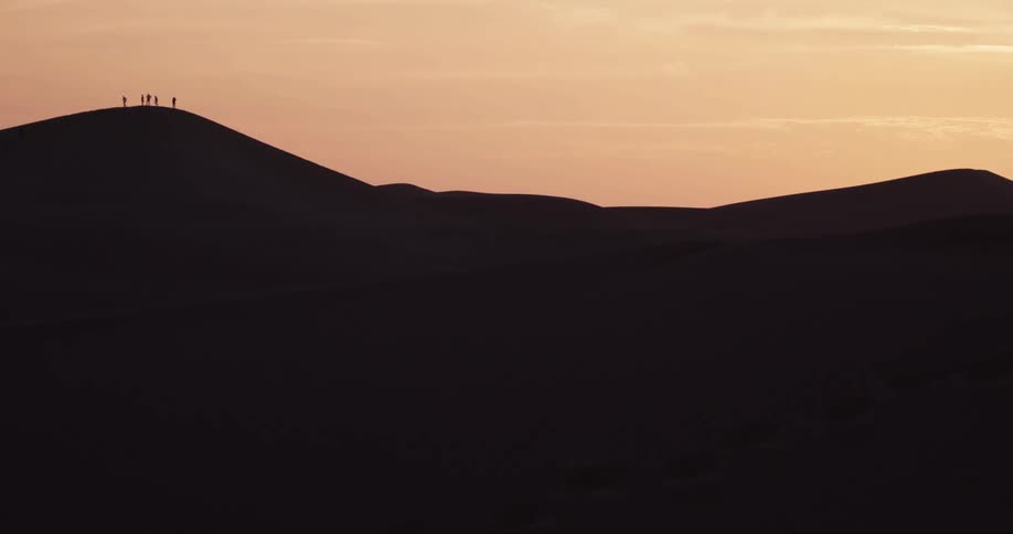 Silhouette of mountains and people on the peak against a reddish sky