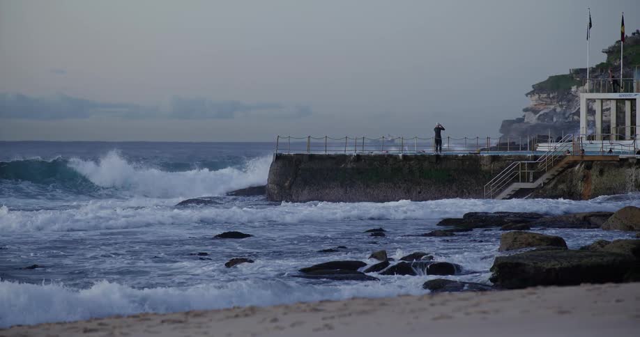 Landscape of a beach with strong waves and a person on a rocky dock in the background