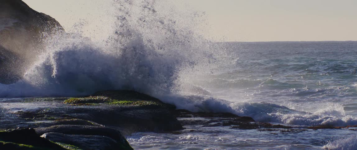 A sea wave breaking on a rock on a coast and causing a lot of water to rise upwards