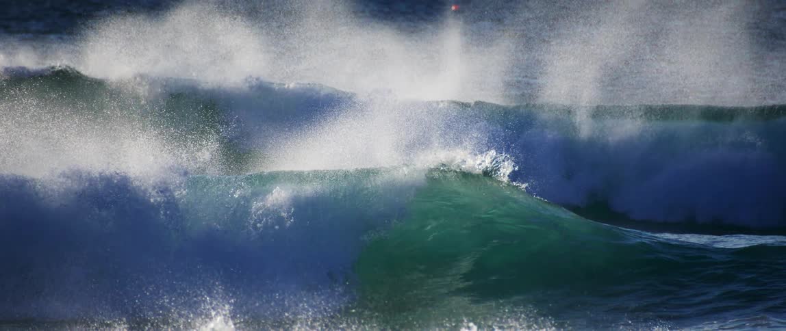Large powerful waves in the ocean with the crest being blown by the wind