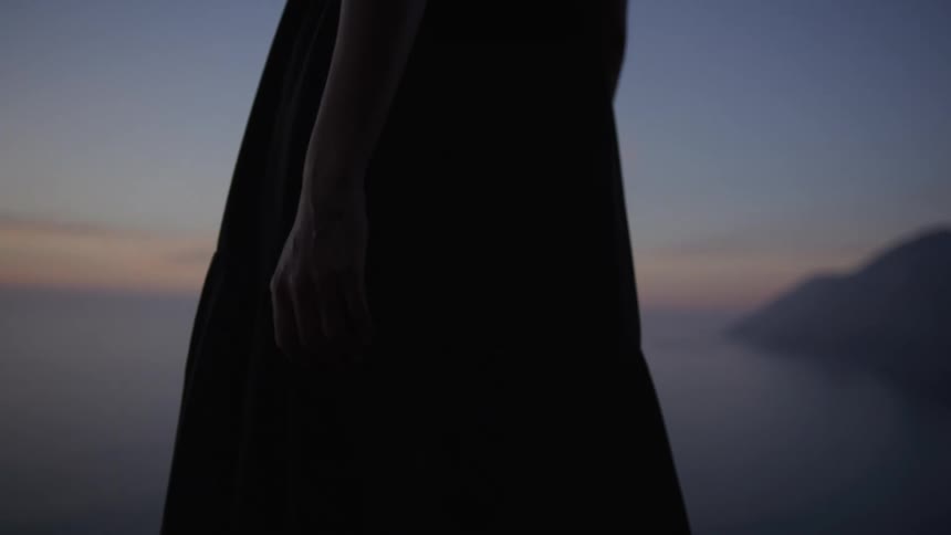 Woman in long dress at a seaside location on a purpletoned sunrise