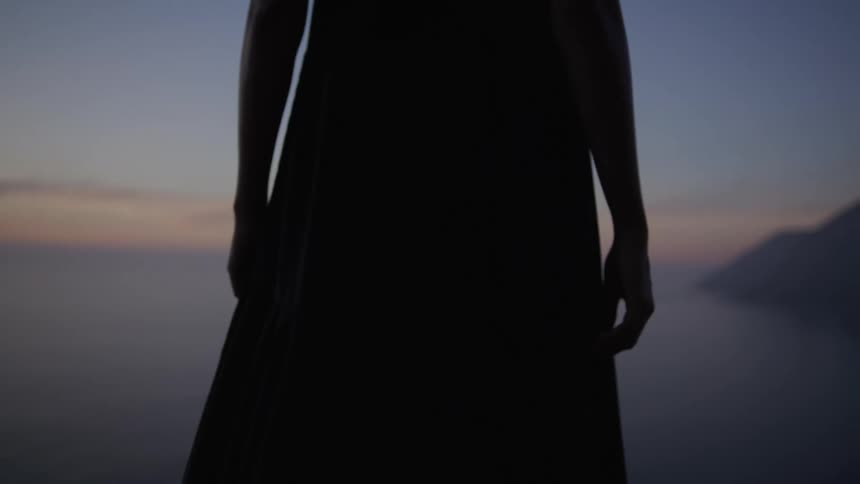 Woman wearing a long dress overlooking a seaside landscape on a morning with a dark sky in shades of purple