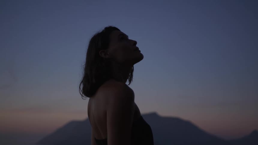 Woman in dress looking up while standing in natural surroundings on a sunrise with purple hues