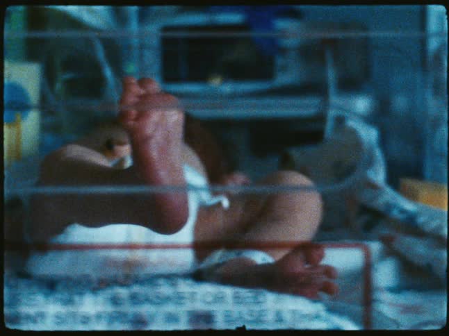 Baby lying in a hospital bassinet raisestheir arm and foot
