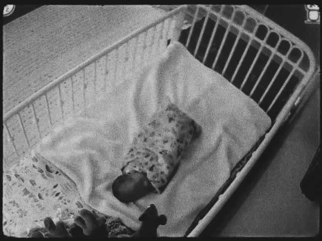 A little baby is sleeping in a crib seen by a black and white security camera