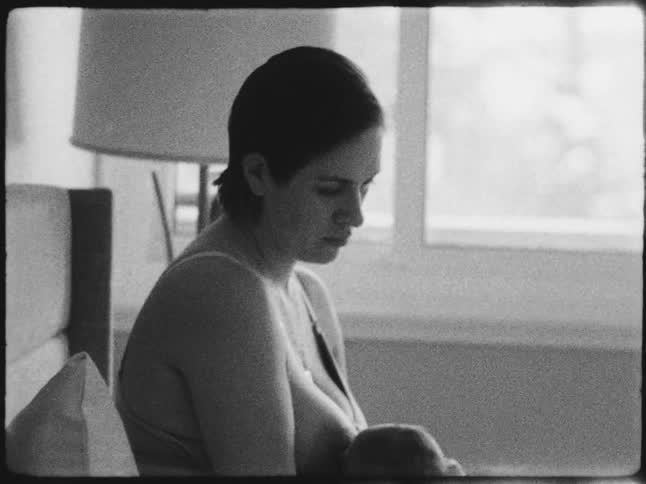 A woman is breastfeeding her baby and she is sitting down and the tones are black and white