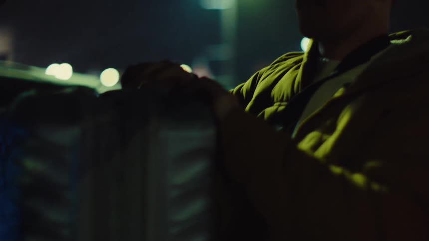 A person in a hoodie prepares a bag in the low light of the night