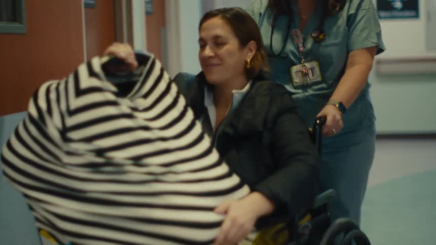 A patient sat in a wheelchair pushed by a nurse through the hospital