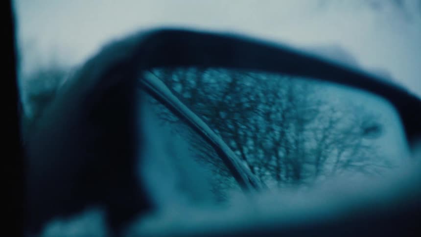 Closeup of a moving cars rearview mirror with snow reflecting off trees in the morning