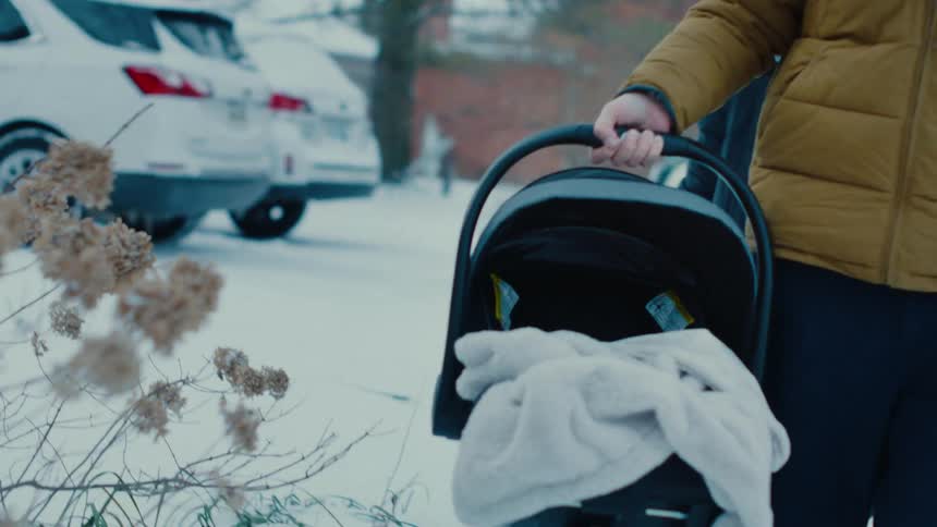 Person wearing puffy jacket carrying an infant carrier across snow covered parking lot