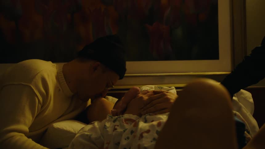 A father kissing his wife as she holds newborn baby while lying on a bed