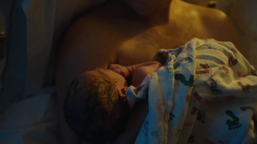 Father sitting on bed with newborn baby on his lap