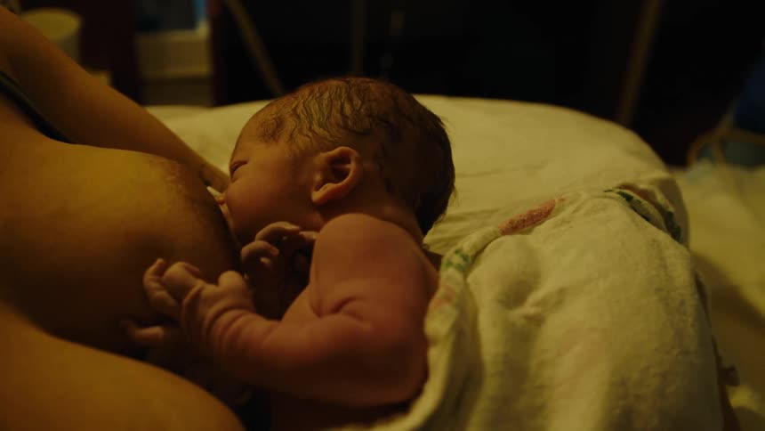 A newborn is gently breastfeeding enveloped in warmth and light