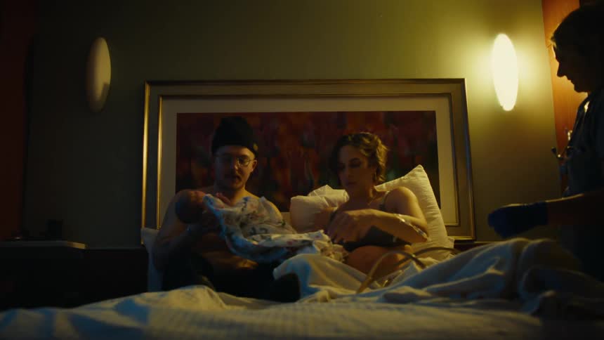 Father holding newborn baby in his arms while sitting next to his wife and a nurse nearby