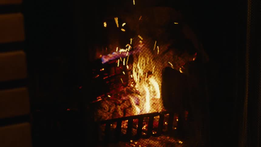 Closeup of logs being moved over a fireplace at night