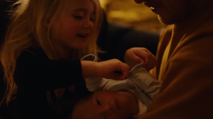 Father with a newborn baby on his lap next to the mother and her other small daughter adjusting the babys pajamas