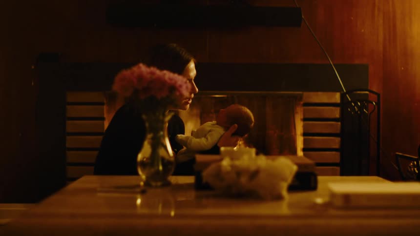 A mother talks to and rocks her child in front of a fireplace