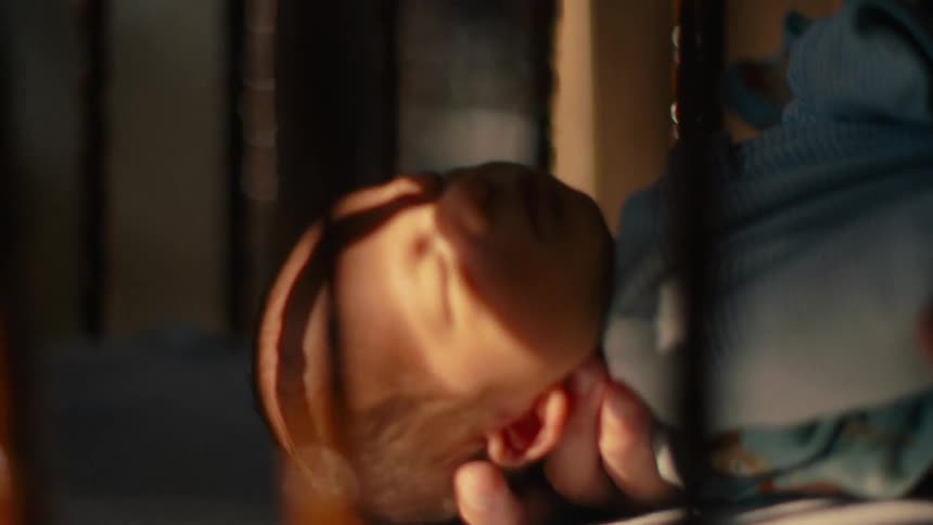 An adults hand carrying a sleeping newborn and placing him in the crib