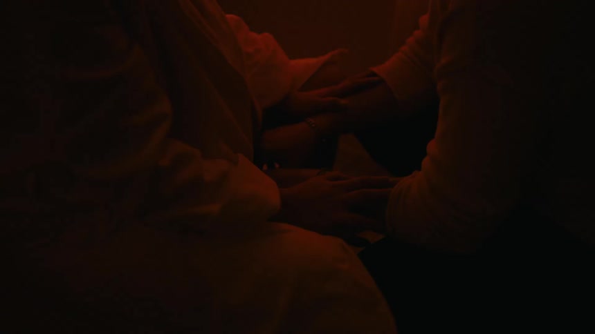 Hands of a man sitting with a pregnant woman breathing deeply having contractions in a dark room