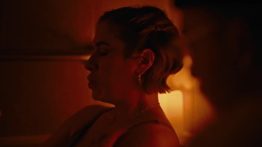 Woman breaths in and out slowly while man holds her shoulder in a dimly lit room