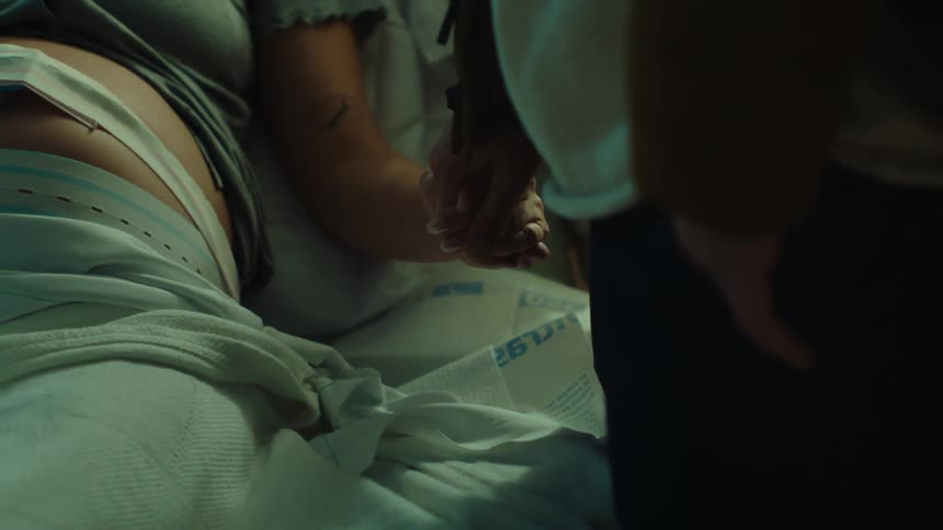 Close up of joined hands of a man and a pregnant woman lying in the hospital on a stretcher