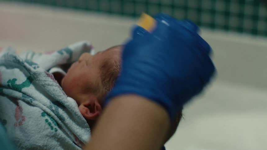 A person wearing blue gloves is rubbing a newborn babys head to clean it