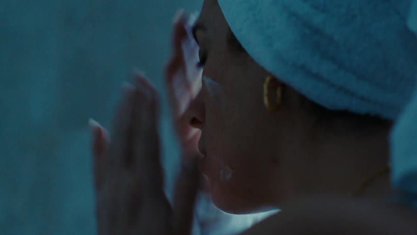 Woman with a towel on her head applying cream to her face