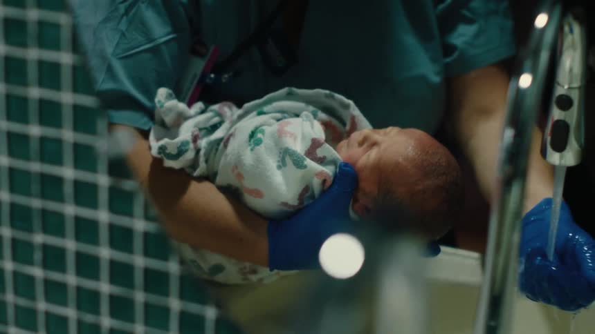 Newborn baby being held by a person wearing blue gloves and medical clothing who is washing his head