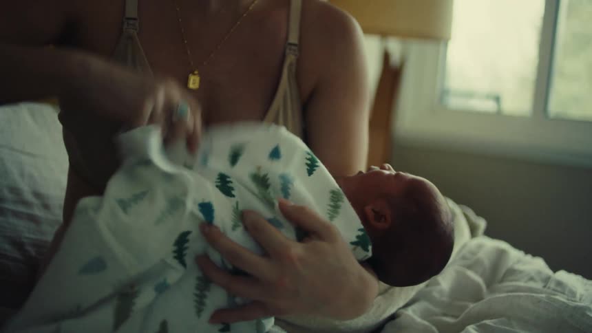 Mother with a newborn baby on her lap placing a blanket around him