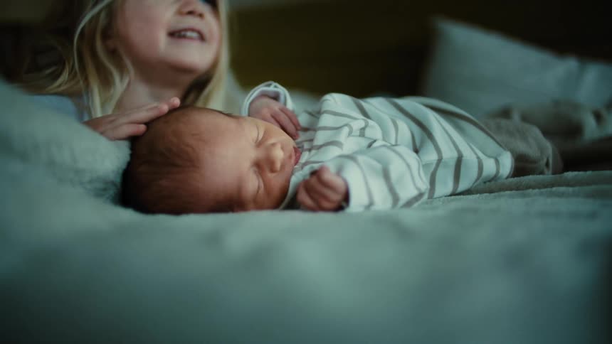 Little blonde girl stroking the head of a newborn baby