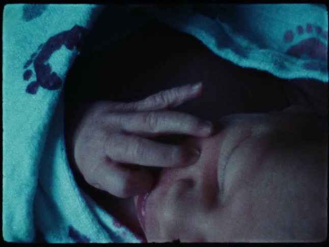 Baby bundled in a blanket touches their face in their sleep