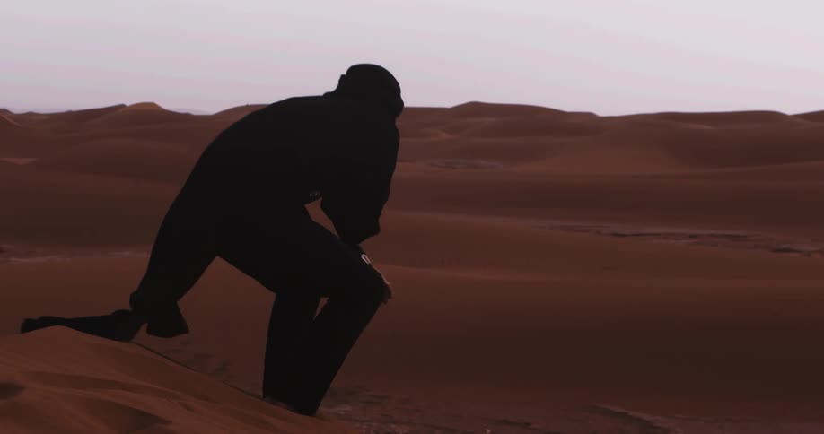 Person in a black burqa sitting and standing on a sand dune