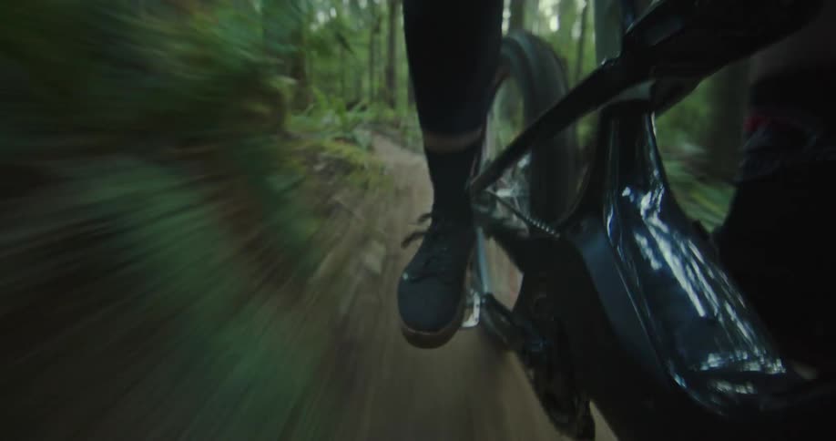 Feet of a person riding a mountain bike at high speed down a forest trail